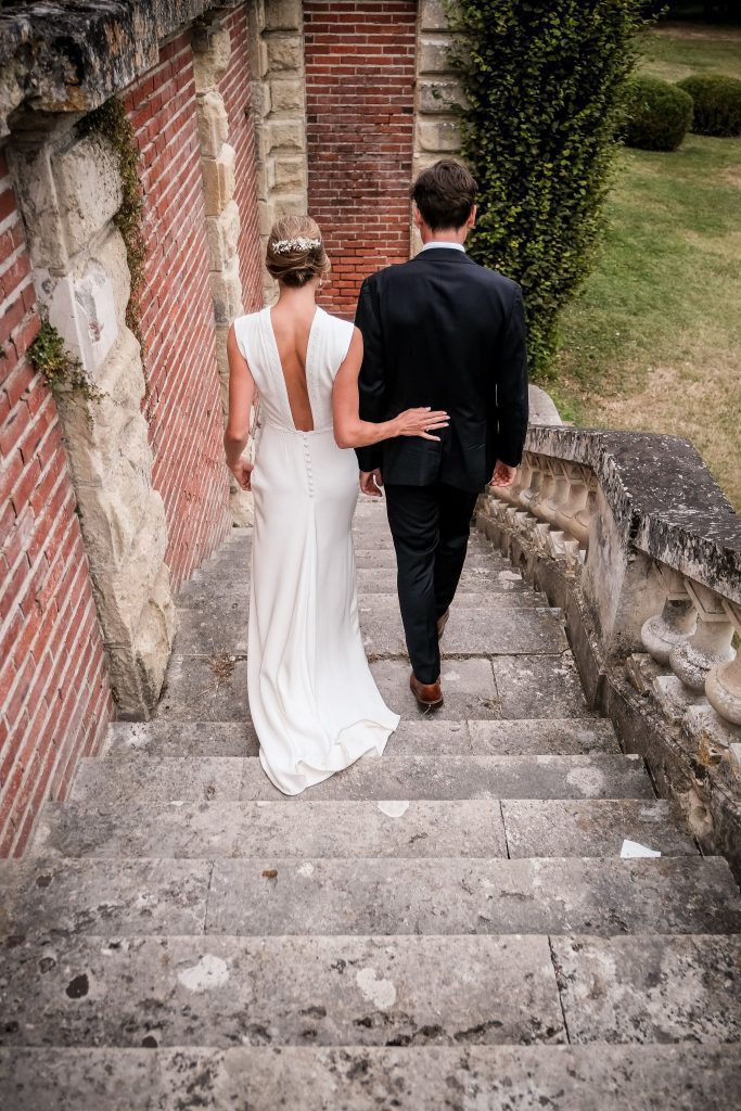 Couple de mariés de dos descendant un vieux escalier extérieur.