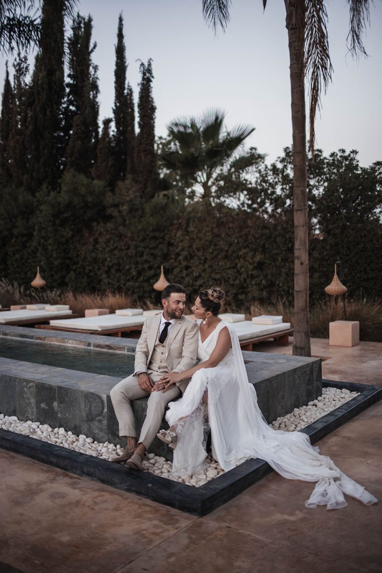 Couple de mariés assis sur le bord d'un bassin. Ils se regardent et la femme enlace légèrement son maris.