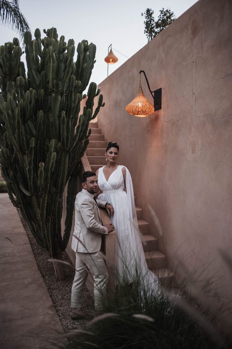 Couple de mariés regardant la camera, la femme est debout dans un escalier et l'homme accoudé au bord de celui-ci.