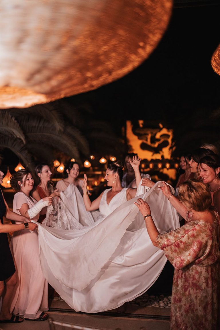 Invitées d'un mariage tenant chacune un bout de la robe de la mariée afin de la faire voler.