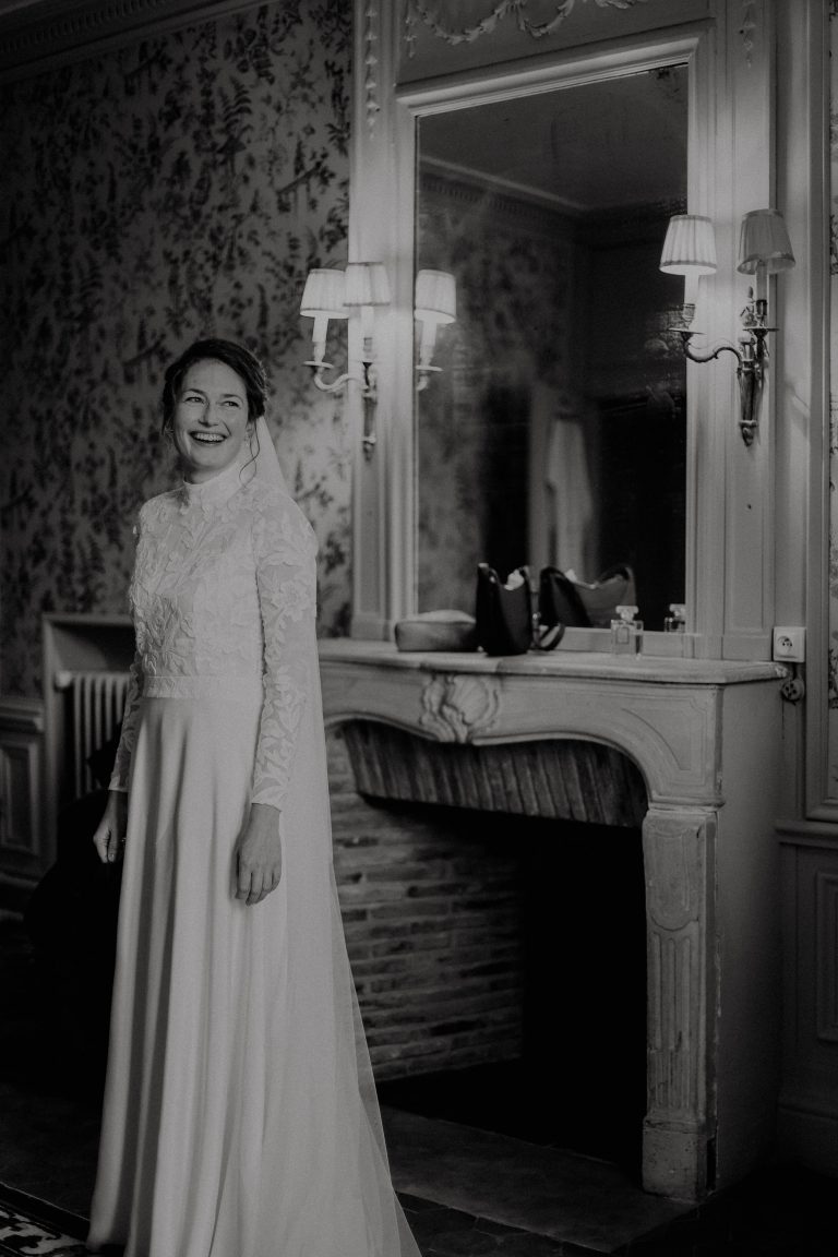 Femme debout en robe de mariée devant une cheminée.