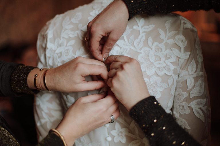 Quatre mains attachant les boutons dans le dos d'une robe de mariée.