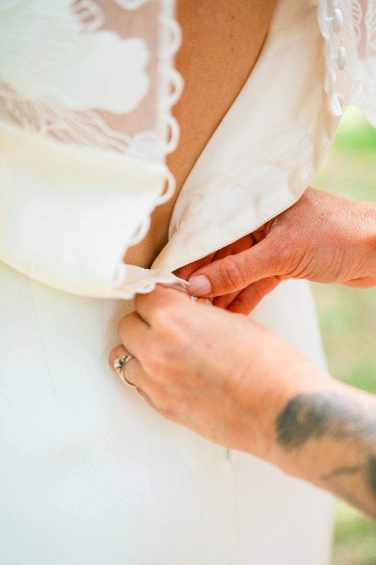 Détail de mains attachant le dos d'une robe de mariée.