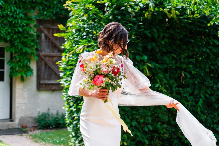Mariée un bouquet à la main réajustant la traine de sa robe Maison Jasmée.