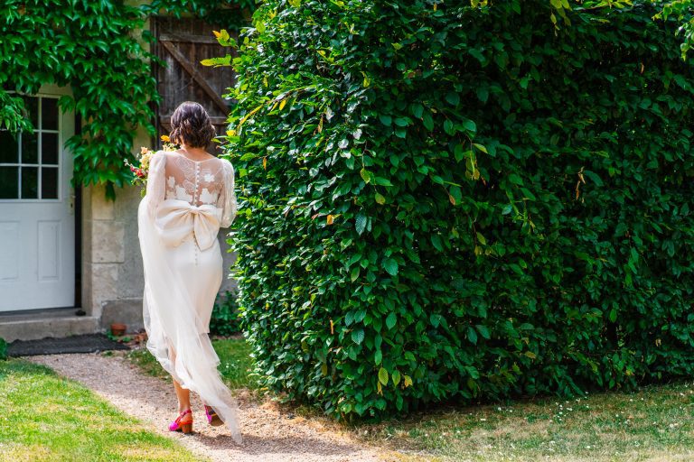 Mariée de dos marchant dans une allée.