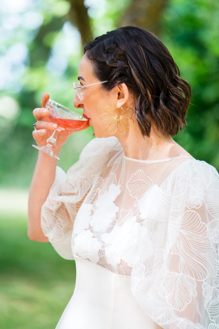 Mariée en robe Maison Jasmée buvant un verre.