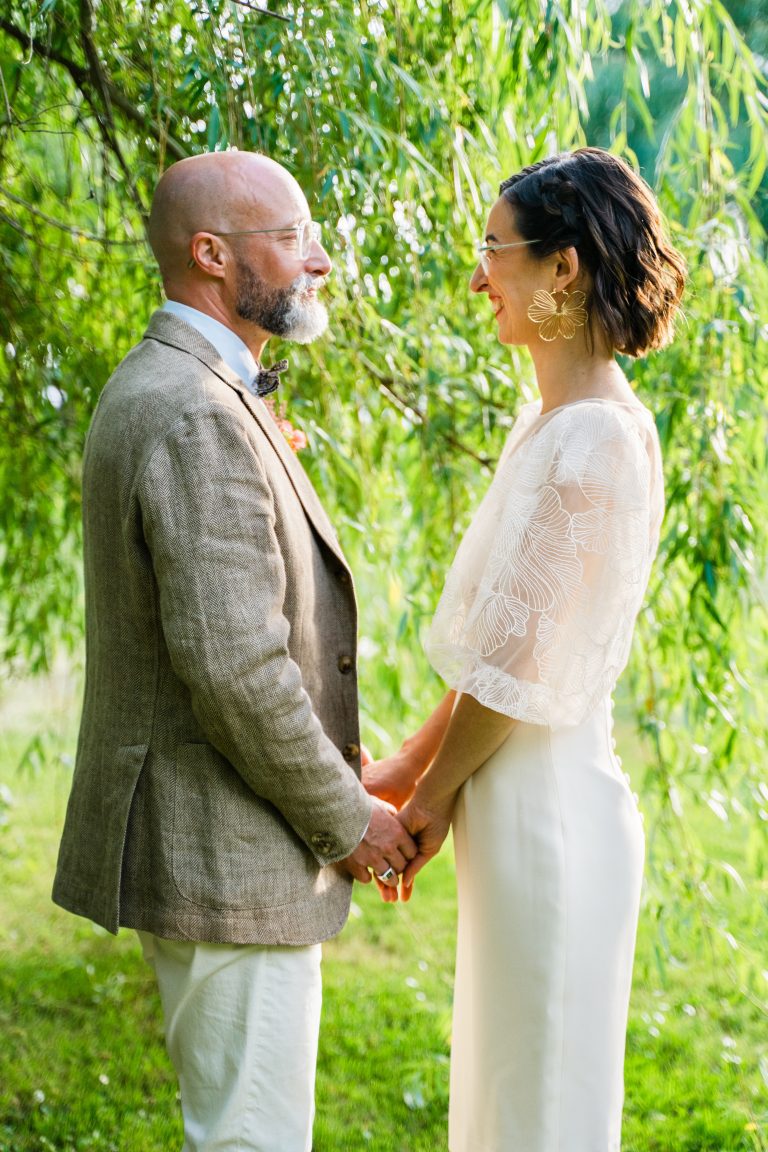 Portrait photo d'un couple de mariés. Ils se tiennent les mains et se regardent dans les yeux.