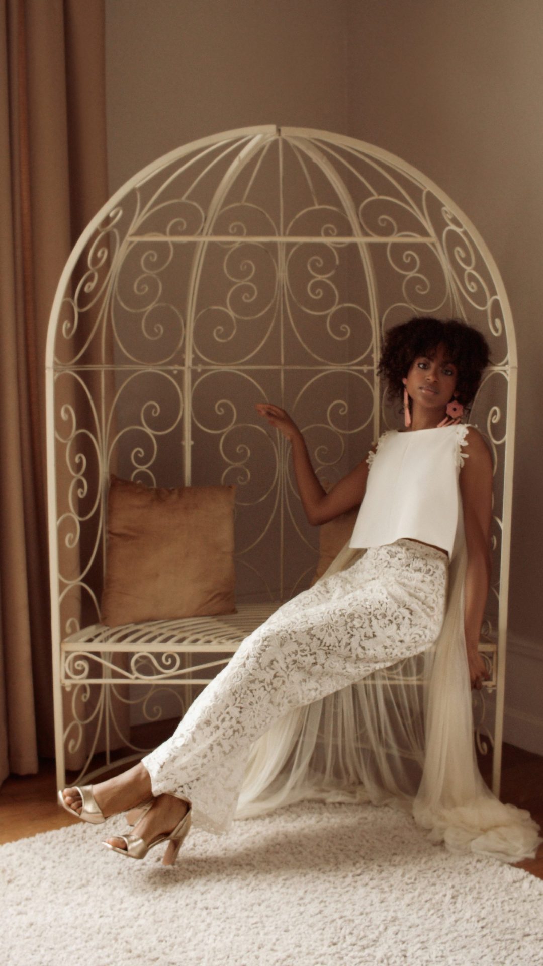 Femme assise. Elle porte l'ensemble Maison Jasmée, composé d'un top et d'un pantalon en guipure.